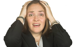A woman in a suit holding her head with both hands.